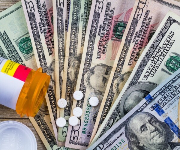 Pills spilled out from a prescription medicine vial, on top of 100 and 50 dollar bills