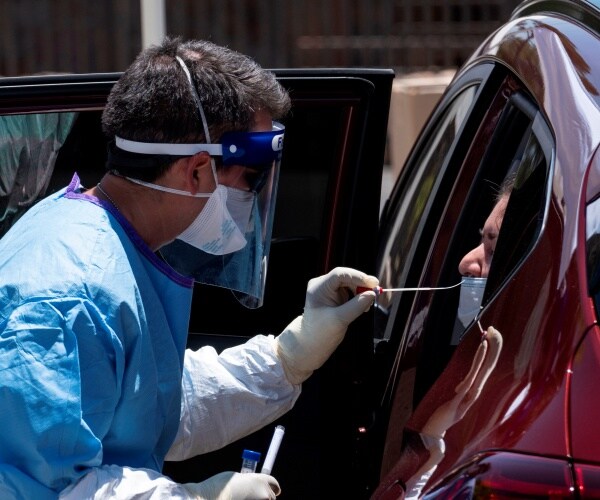 national guardsman in a blue protective suit tests a woman for covid