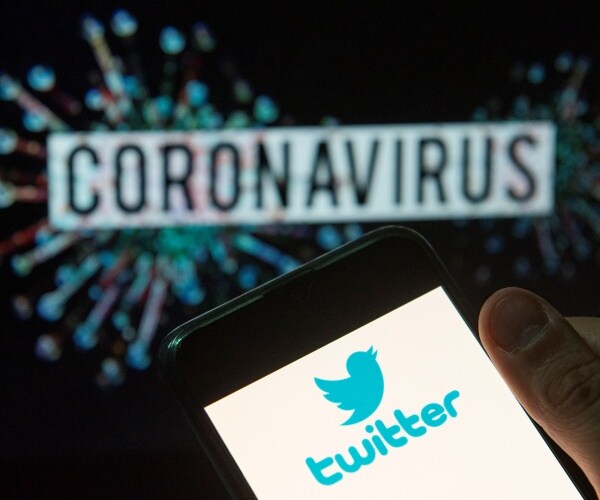 person holding smart phone with twitter icon on it with coronavirus in the background