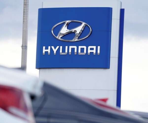 the hyundai company logo hangs over a long row cars