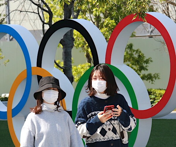 two masked girls walk past the Olympic rings in Tokyo, japan