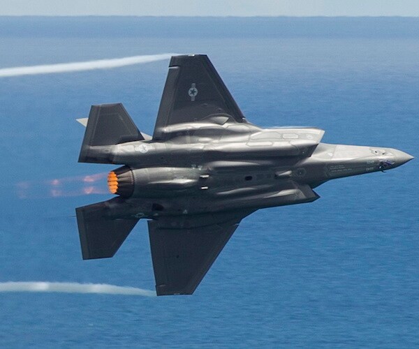 an eff thirty five banks left, showing its undercarriage in flight over the pale blue sky