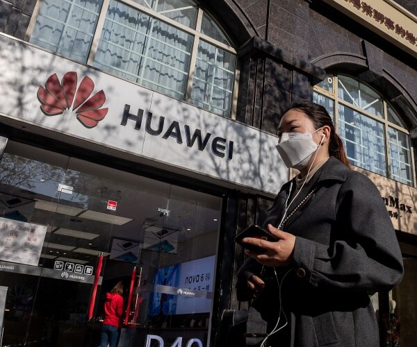 woman in a black coat and face mask walks by a huawei store