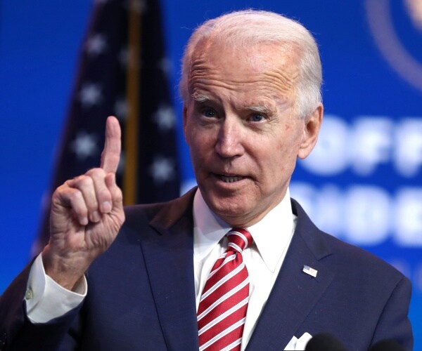 biden in a suit and red striped tie pointing his index finger up
