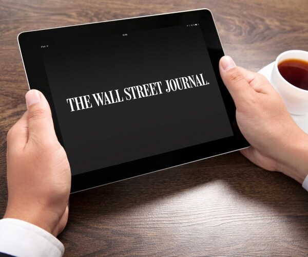 man holds an ipad with wsj logo on it next to a cup of coffee