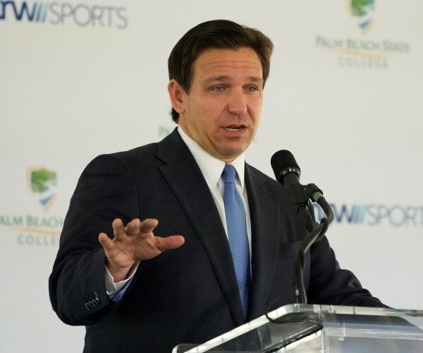 ron desantis gestures while speaking into a microphone