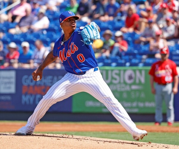 marcus stroman in a blue mets jersey and white striped pants pitching a baseball in front of a crowd