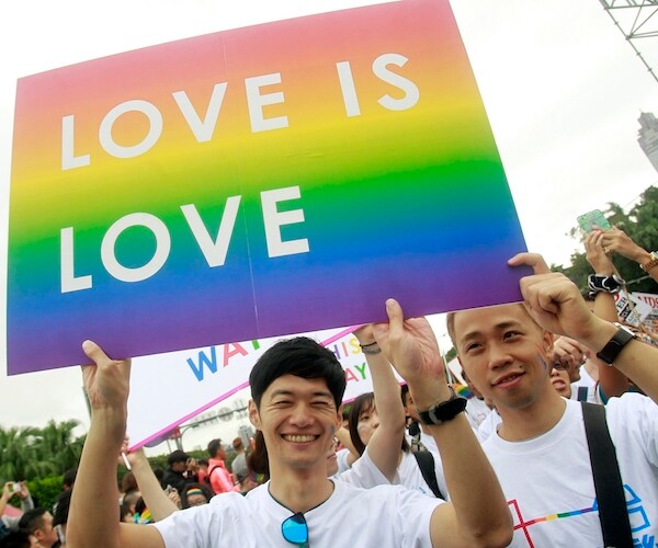 a man raises a rainbow colored banner that reads "love is love"