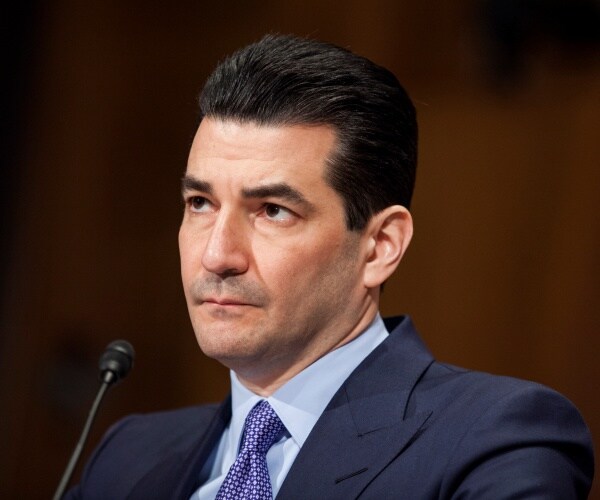 gottlieb in a suit, cobalt blue tie and light blue shirt with a brown background