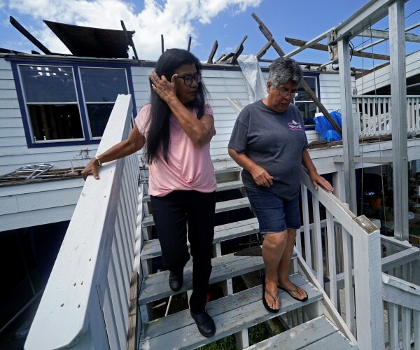 two women examine walk around a damaged house