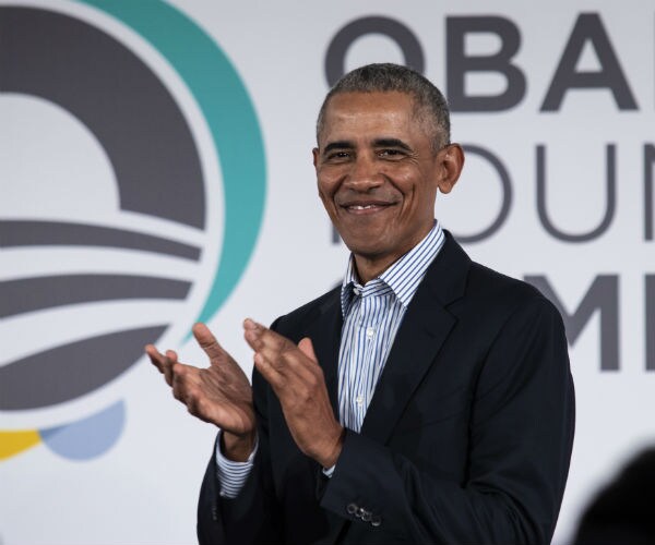 former president barack obama claps his hands while smiling