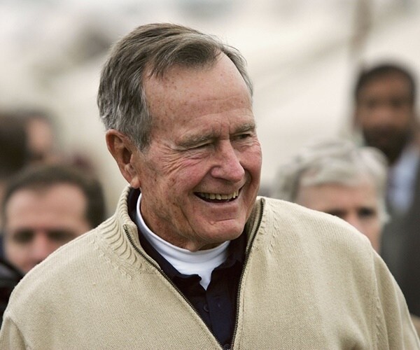 george h.w. bush smiling in front of a slew of onlookers