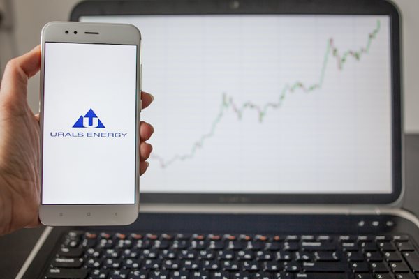 a smart phone showing an energy company logo with a laptop in the background showing rising oil price