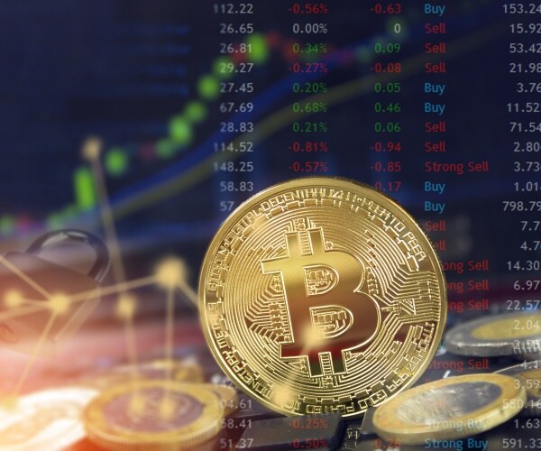 gold coin of bitcoin is shown in front of trading software