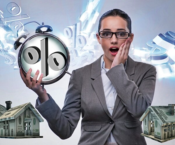 businesswoman surprised about mortgage rates holding clock with percent sign amid houses built of dollars 

