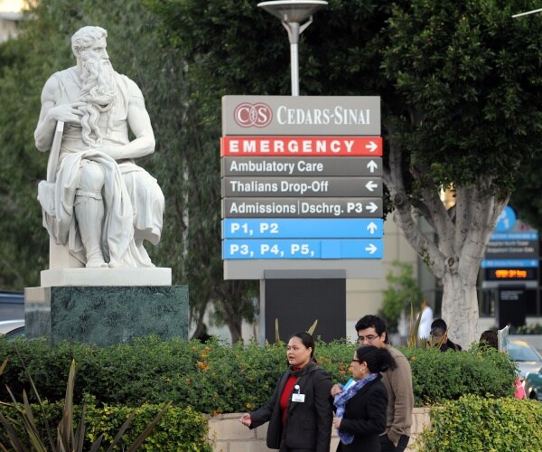 people walk by a sign directing people to cedars-sinai medical center in LA
