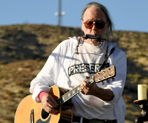 neil young plays his guitar and harmonica on a stage
