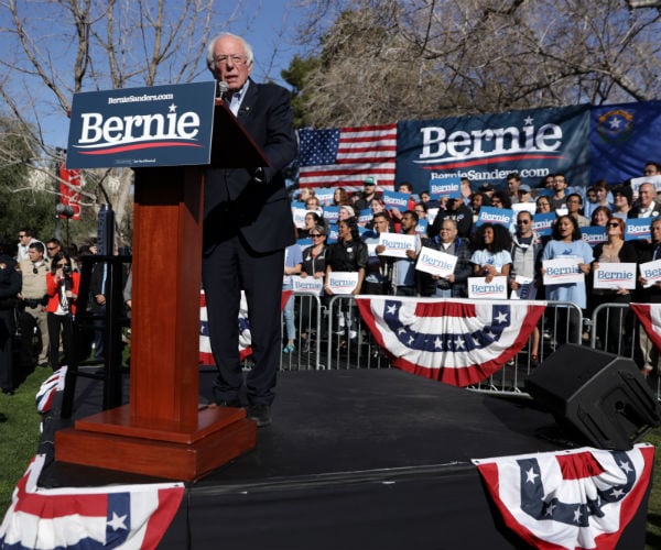 sen. bernie sanders is speaking at a podium displaying his campaign slogan.