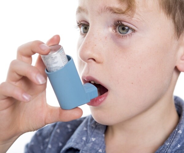 little boy using a blue inhaler for asthma