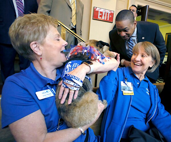 a woman holds a dog who is greeted by a politician and another smiling woman
