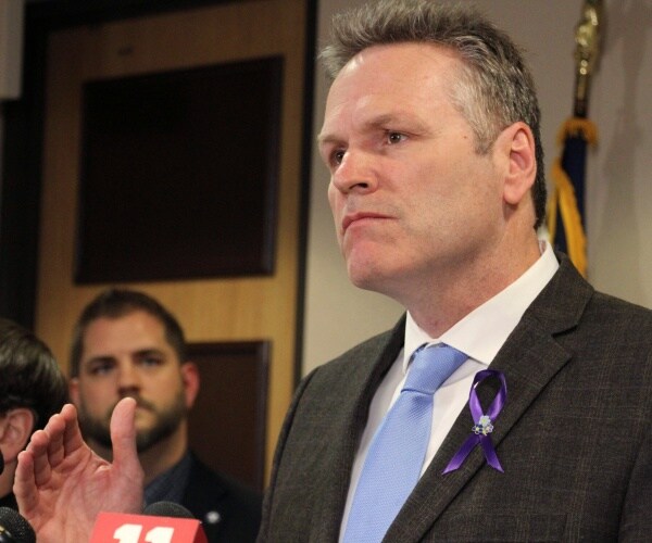 alaska governor mike dunleavy in a light blue tie and gray suit stands during a news conference