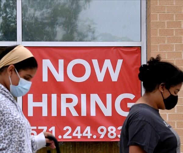 women wearing face masks walk past now hiring sign