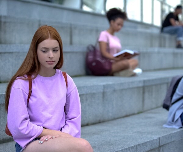 high school student looking sad a depressed, sitting by herself in bleachers
