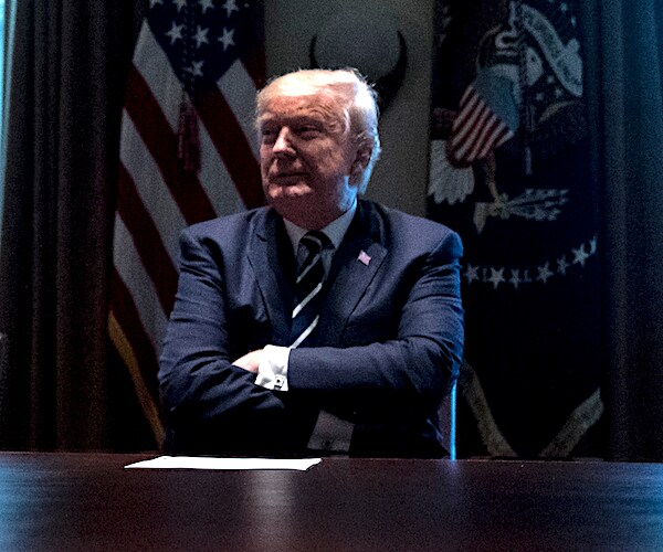 president donald trump sits at the cabinet table with his arms folded