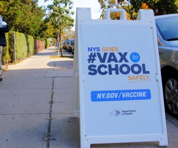 a nyc vaccination signs sits on the sidewalk.