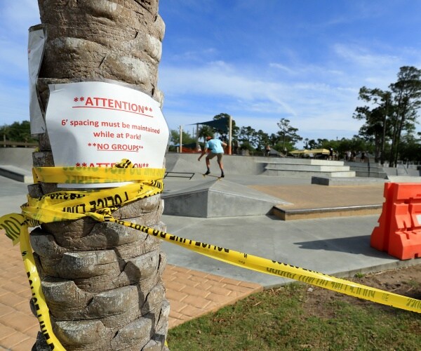 caution tape and a sign telling people to socially distance on a palm tree with a person skating in a park
