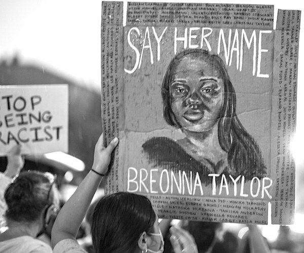 a breonna taylor protester holds up a sign with say her name