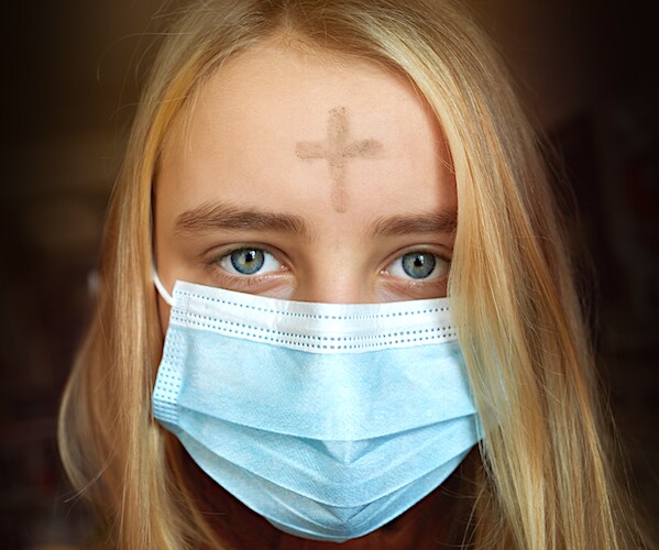 a blonde girl in a face mask has the ash wednesday cross on her forehead