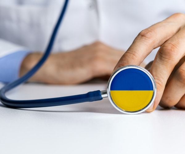 doctor in whites holding stethoscope with Ukraine flag colors on back of it