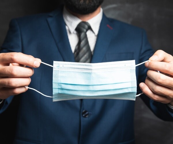 man in suit holding mask he is about to put on