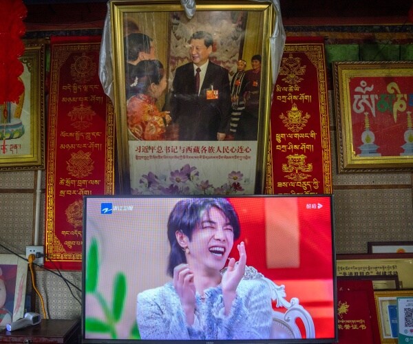 A TV shows a broadcast of a Chinese talk show program as it sits beneath a photo of Chinese President Xi Jinping.