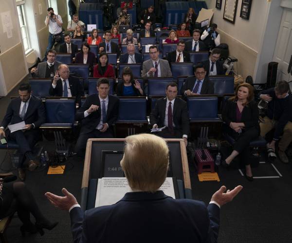 trump seen from the back looking out at the press seated and asking questions