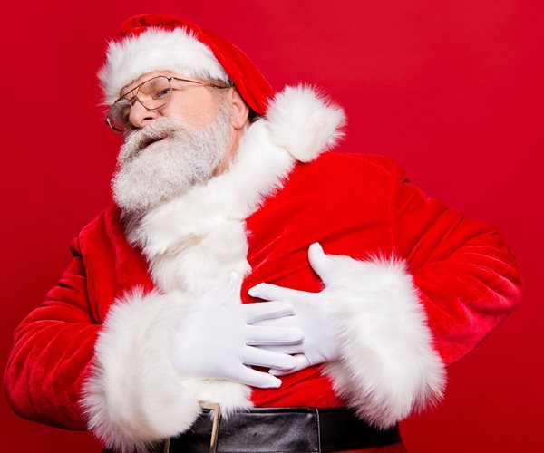 man in santa claus costume grips his chest as if suffering a heart attack