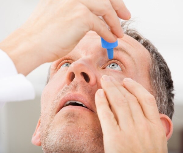 man putting drops in his eyes