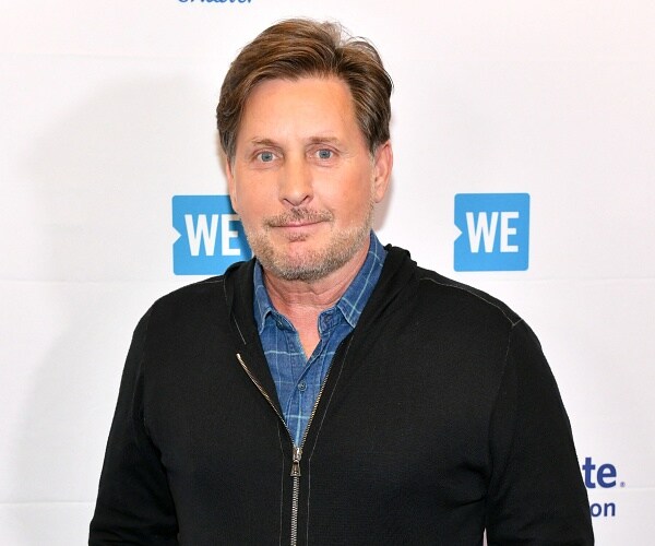 emilio estevez stands in front of photo backdrop 