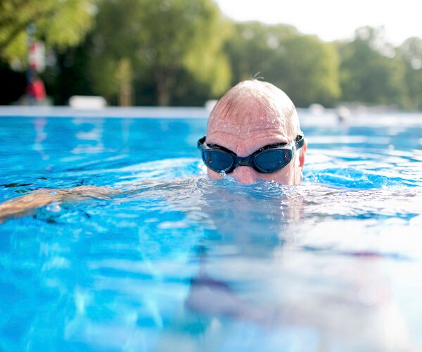 a man ducks his head out of the water in a bright blue swimming pool