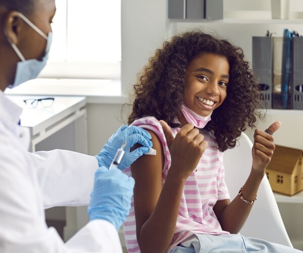 young girl getting vaccine, giving thumbs up