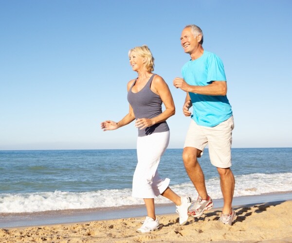 older man and woman smiling and jogging on beach