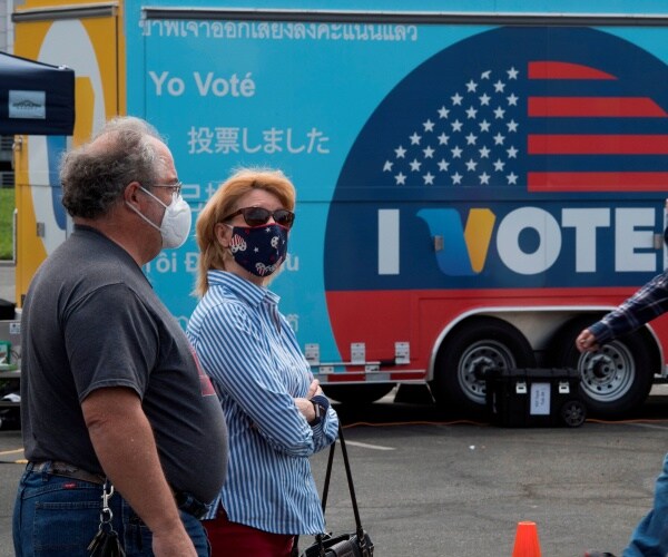 a couple stands in line wearing face masks in front of a truck that has a large "i voted" sign