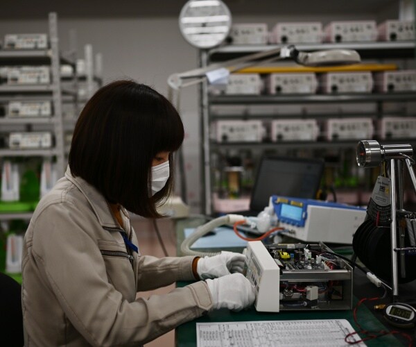 woman wearing a mask and jacket working in a manufacturing plant