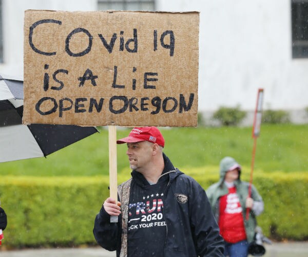 a demonstrator holds a sign that reads covid 19 is a lie open oregon 