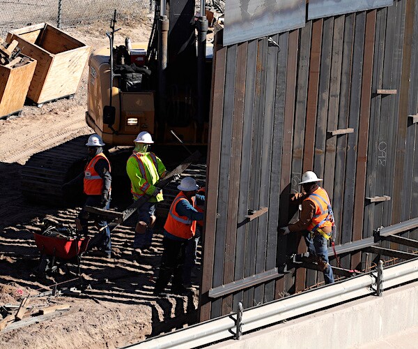 workers place sections of metal wall as a new barrier is built along the texas-mexico border
