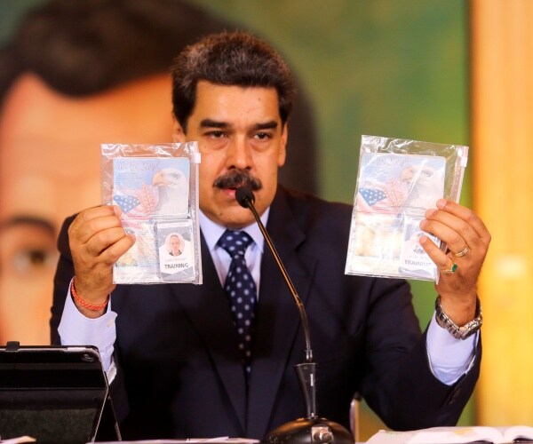 Maduro holds up two laminated id pictures and documents of luke denman and airan berry