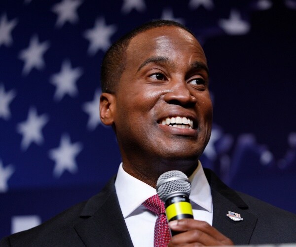 john james in a black suit speaking into a mic