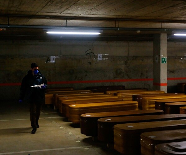 worker wearing a face mask checks coffins at a funeral home