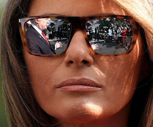 melania trump looks on wearing sunglasses which reflect president donald trunp while addressing the media